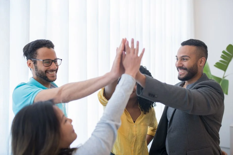 Office scene with diverse colleagues around a stressed woman holding a sign that says HELP. Focus on teamwork dynamics.