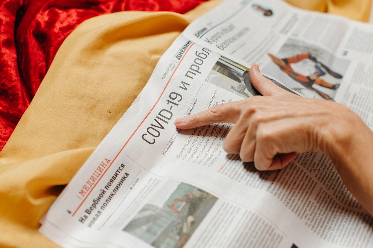 Un gros plan montre une main pointant un titre sur la COVID-19 dans un journal.